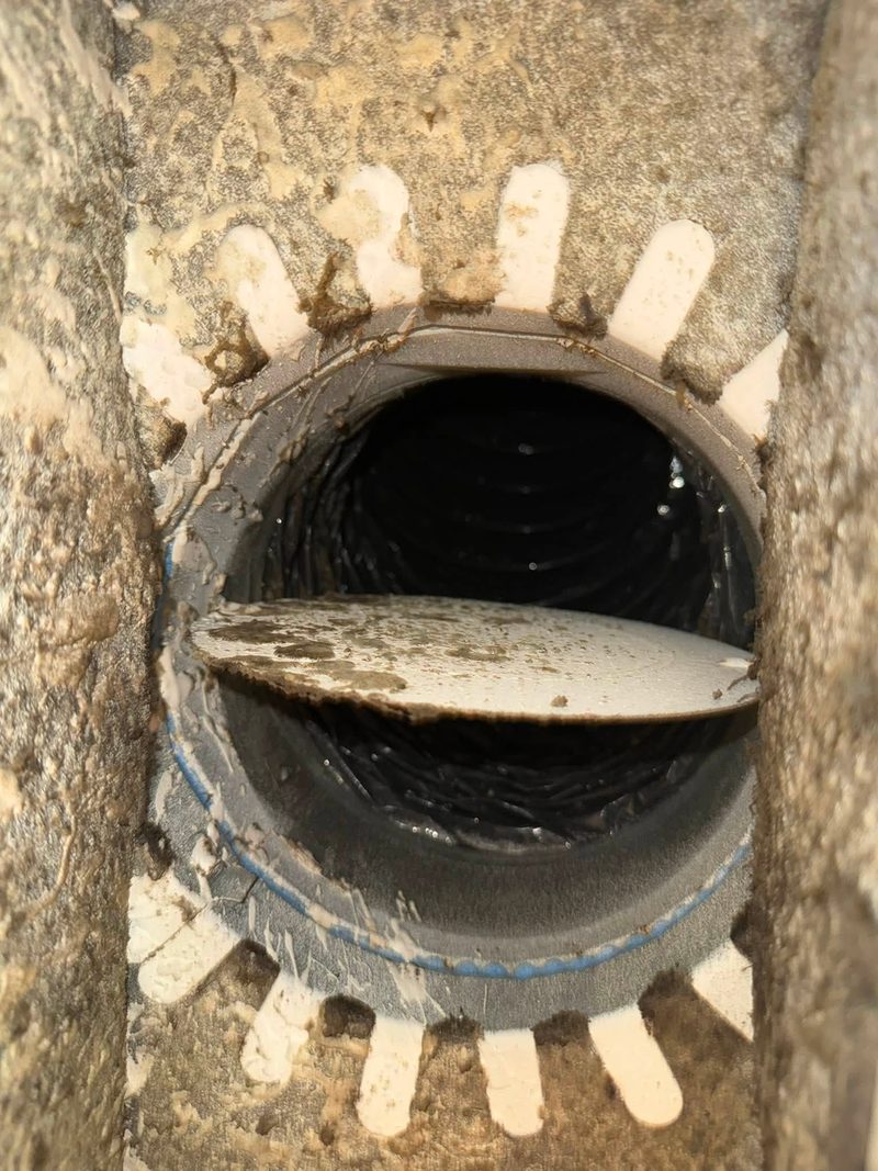 Round duct interior showing a damper blade coated in debris