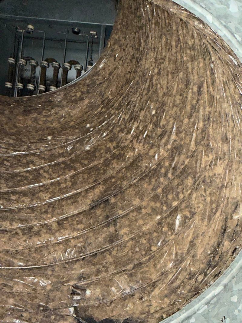 Interior of a round supply duct with heavy dust accumulation before cleaning