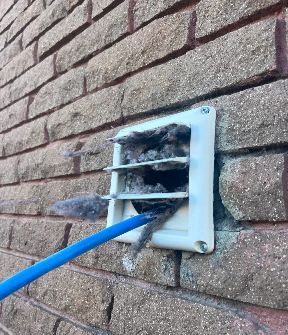 Technician clearing a dryer vent termination on an exterior wall