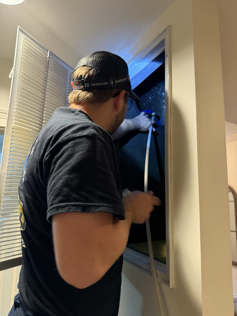 Technician cleaning a ceiling supply register from inside the unit